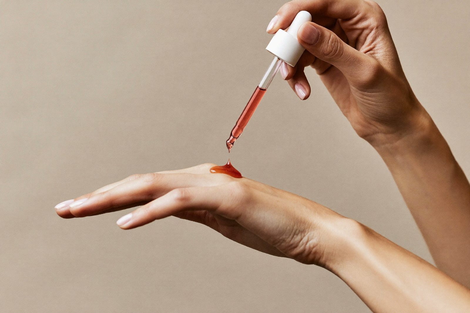 Editorial beauty photo: dropper releasing a drop of coral-pink PDRN serum onto a hand