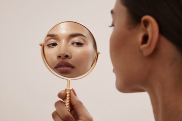 Editorial beauty photo: woman checking her skin in a handheld mirror for the skin type quiz